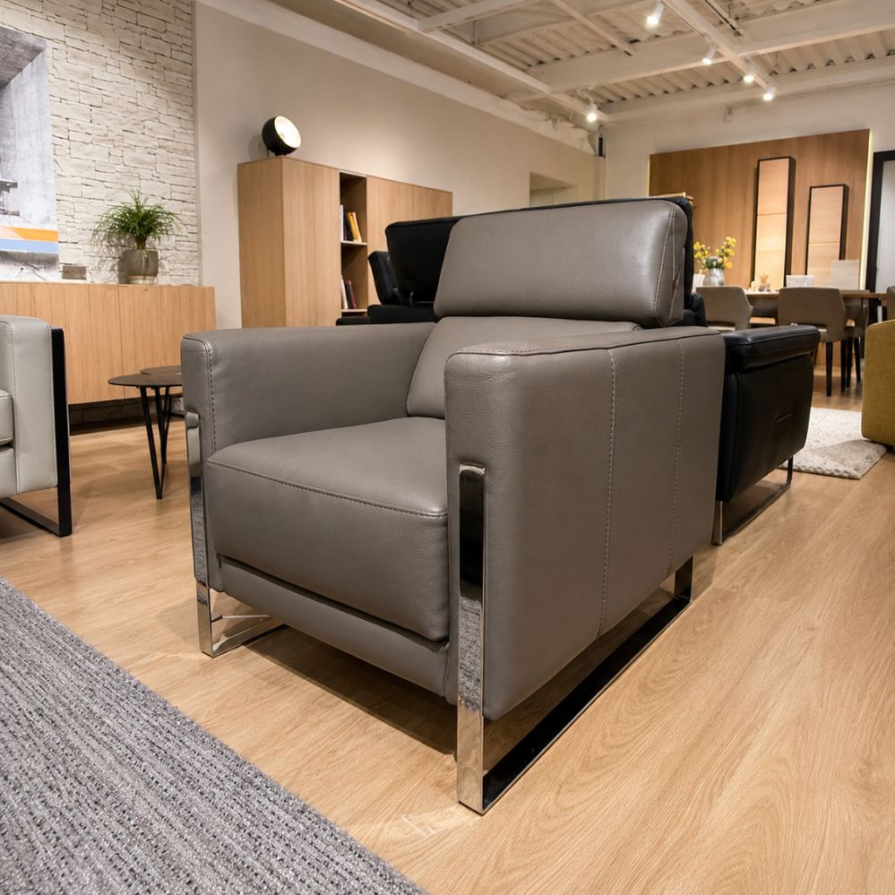Schuin vooraanzicht van de Calia Italia Annie E24 fauteuil in taupekleurig leder met blinkend metalen onderstel – toonzaalmodel Sint-Gillis-Waas – Verberckmoes