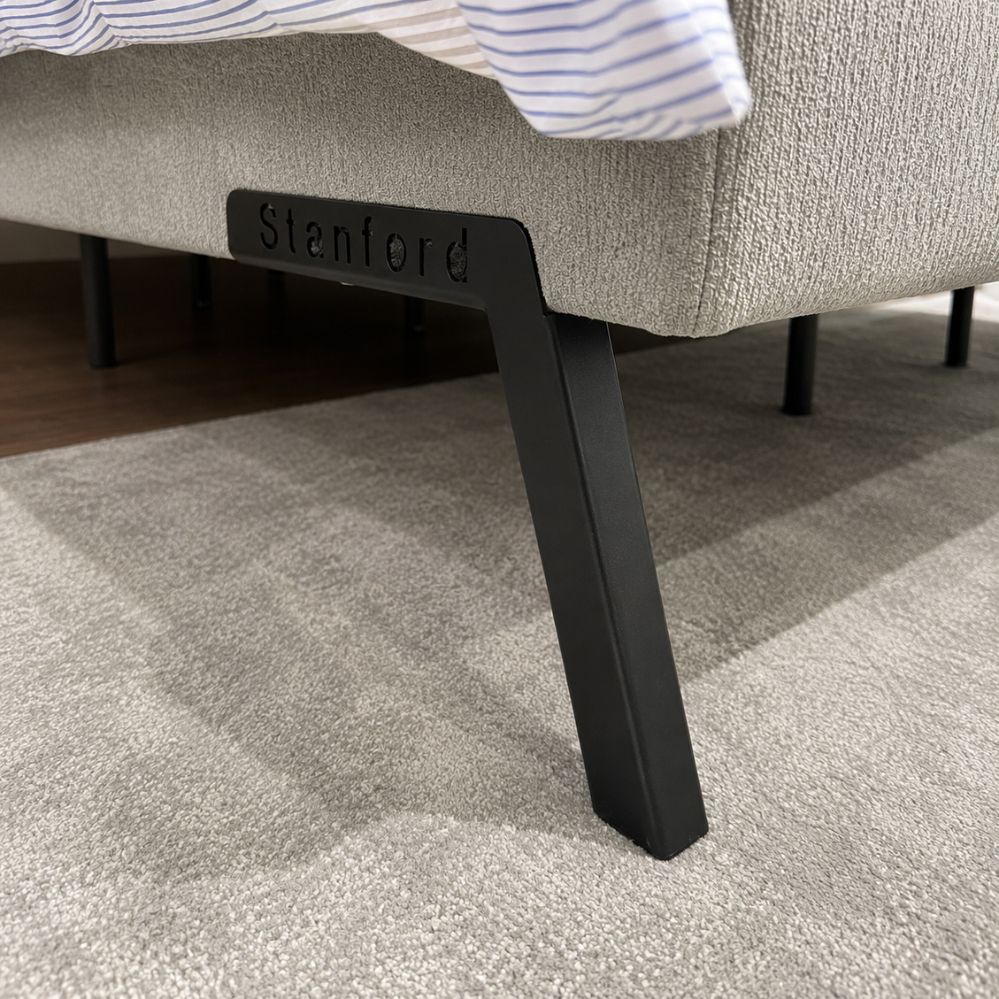 Detail van de zwarte schuine poot met Stanford-logo onder de lichtgrijze Luna XL boxspring, toonzaalmodel Sint-Gillis-Waas – Verberckmoes