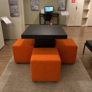 Veldeman Bedding tafel van 80 × 80 cm in zwart kunstleder met 4 oranje stoffen poefjes op wieltjes, toonzaalmodel Sint-Gillis-Waas bij Meubelen Verberckmoes.