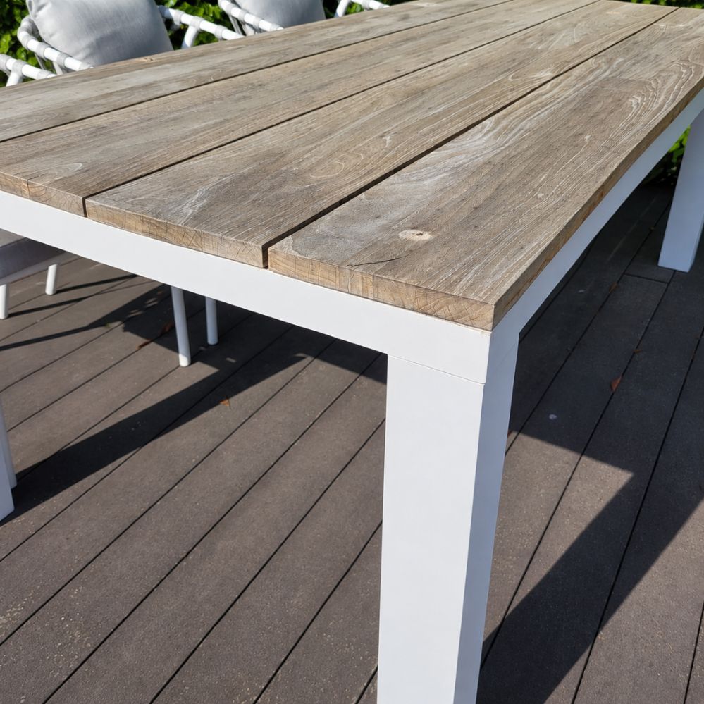 Detail van het Buffed teak tafelblad en het wit mat aluminium onderstel van de Jati Kebon Square tuintafel als terrasmodel in Temse